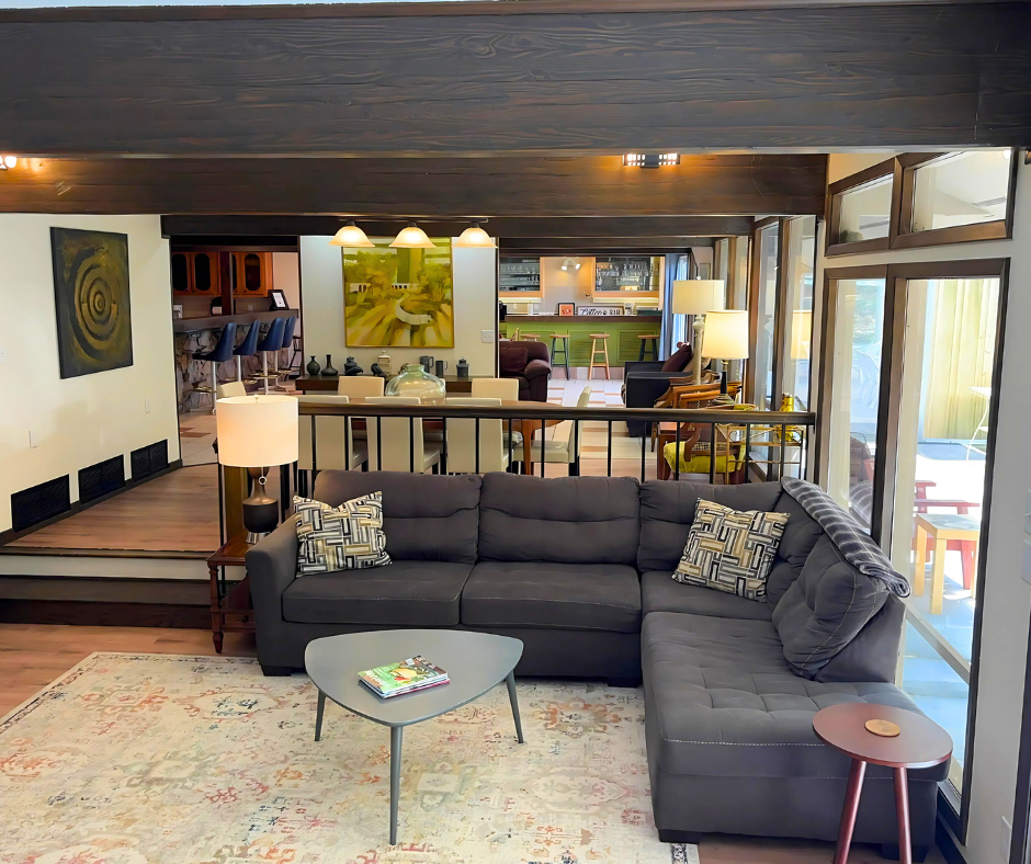 Modern living room with dark sectional sofa, coffee table, rug, and open view to a kitchen/bar area.