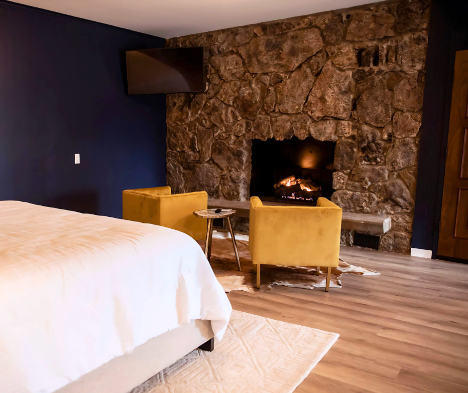 Modern bedroom with stone fireplace, yellow chairs, wood flooring, and a bed in the foreground
