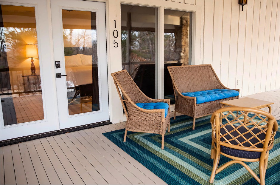 Porch with wicker chairs, blue cushions, striped rug, and glass double doors numbered 105