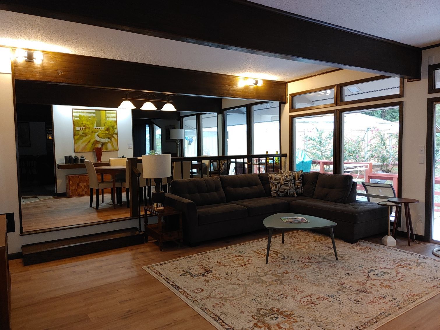 Modern living room with dark sofa, patterned rug, dining area, and large windows opening to a balcony