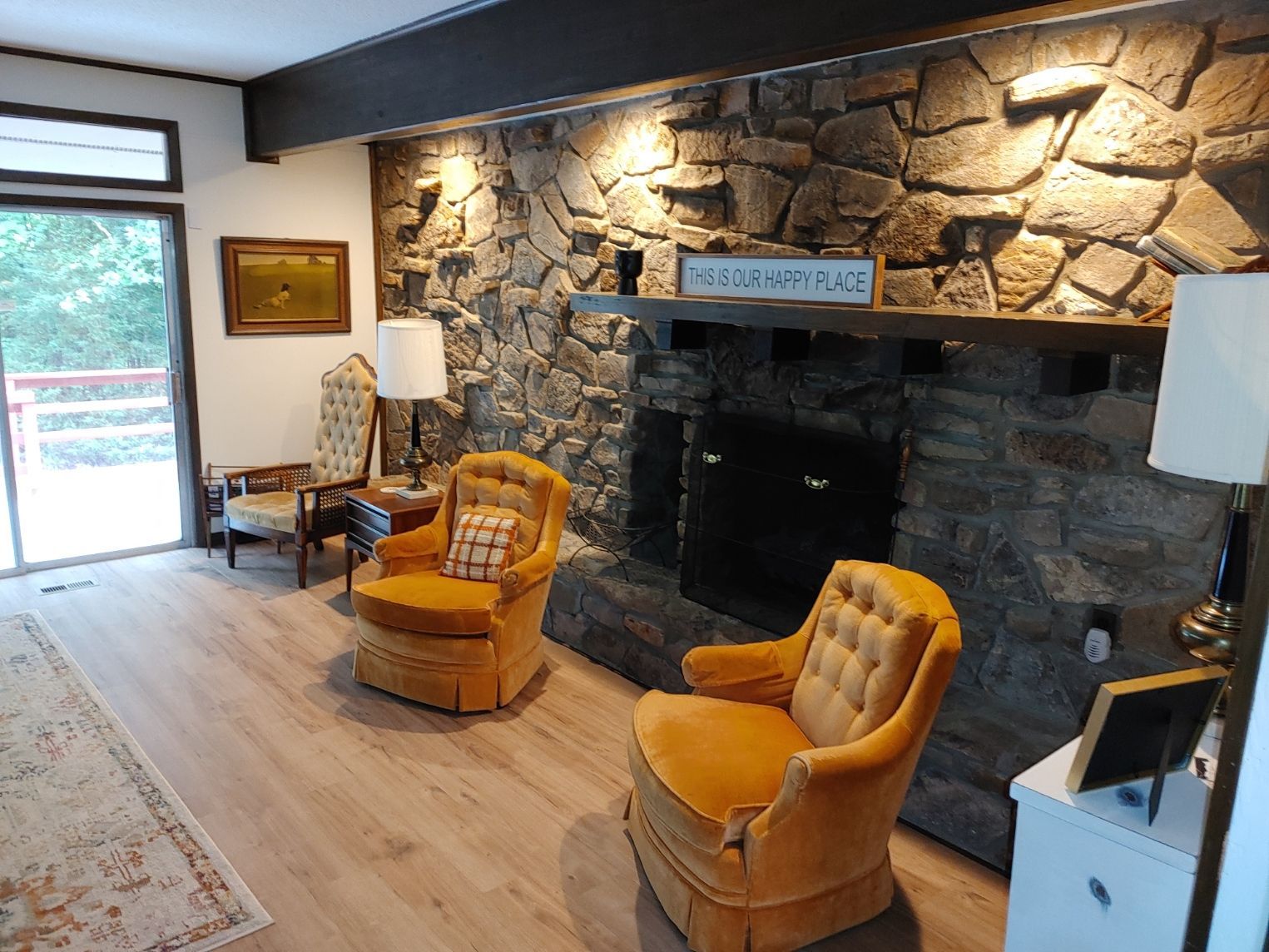 Cozy living room with stone fireplace, two orange chairs, and sliding glass door to a patio
