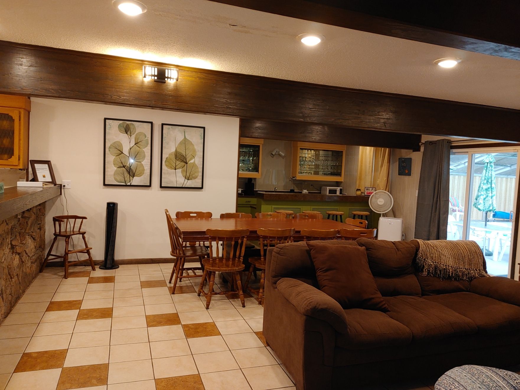 Cozy living room with brown sofa, wood dining table, tiled floor, and large windows at the back