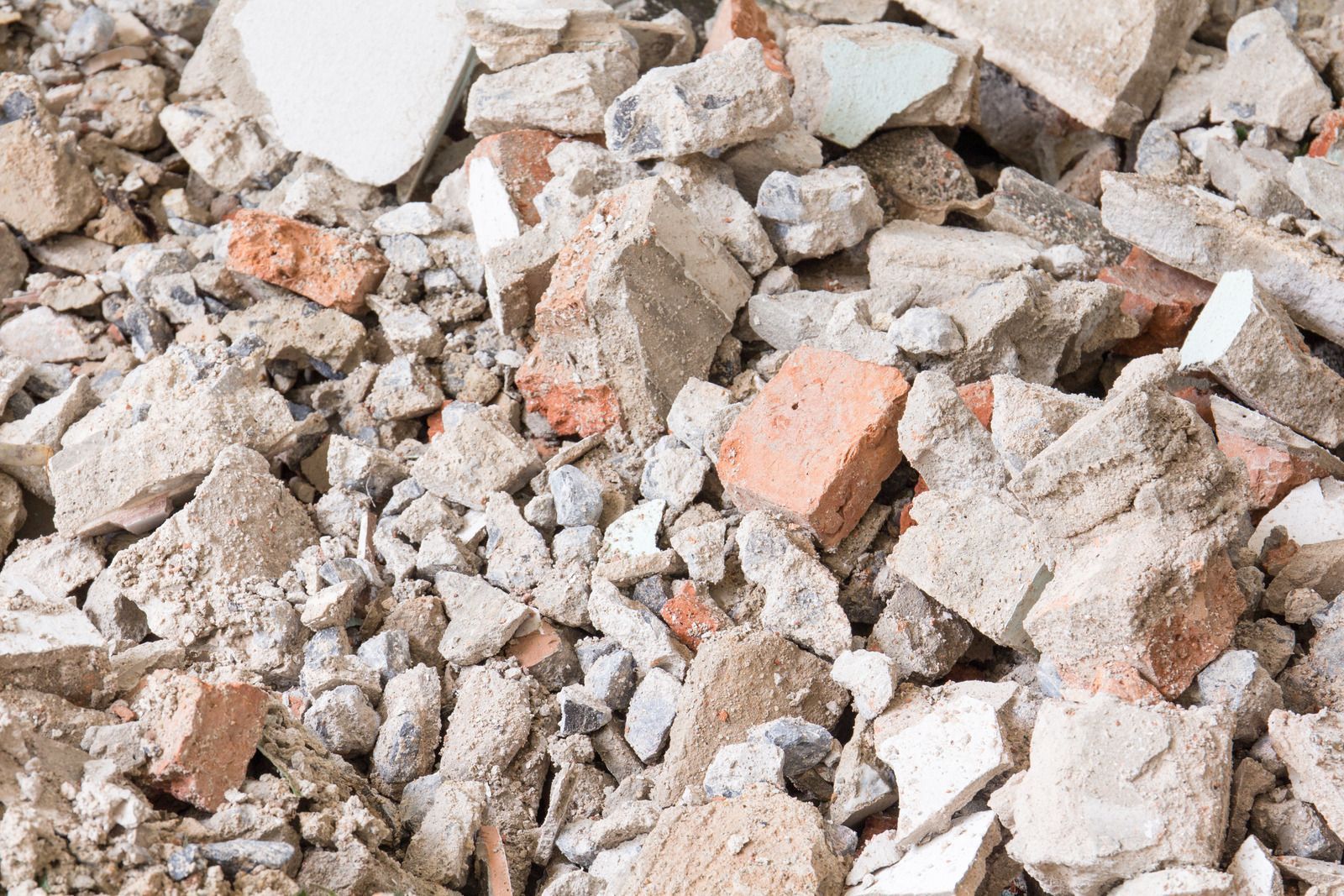 A close-up pile of construction debris, featuring broken concrete, mortar, and fragments of reddish-orange bricks.