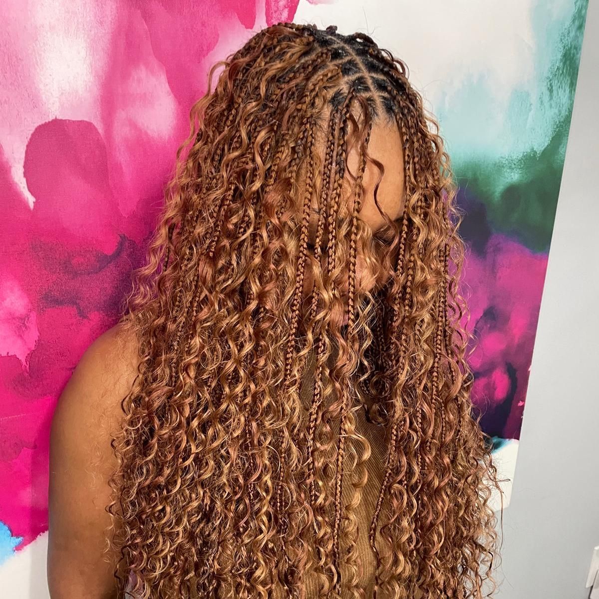 Person with long curly blonde hair against a pink, green, and white backdrop
