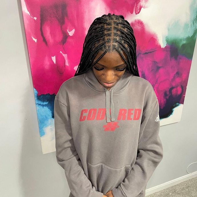 Person in a gray hoodie with red text, looking down, standing before a pink and blue abstract wall art backdrop.