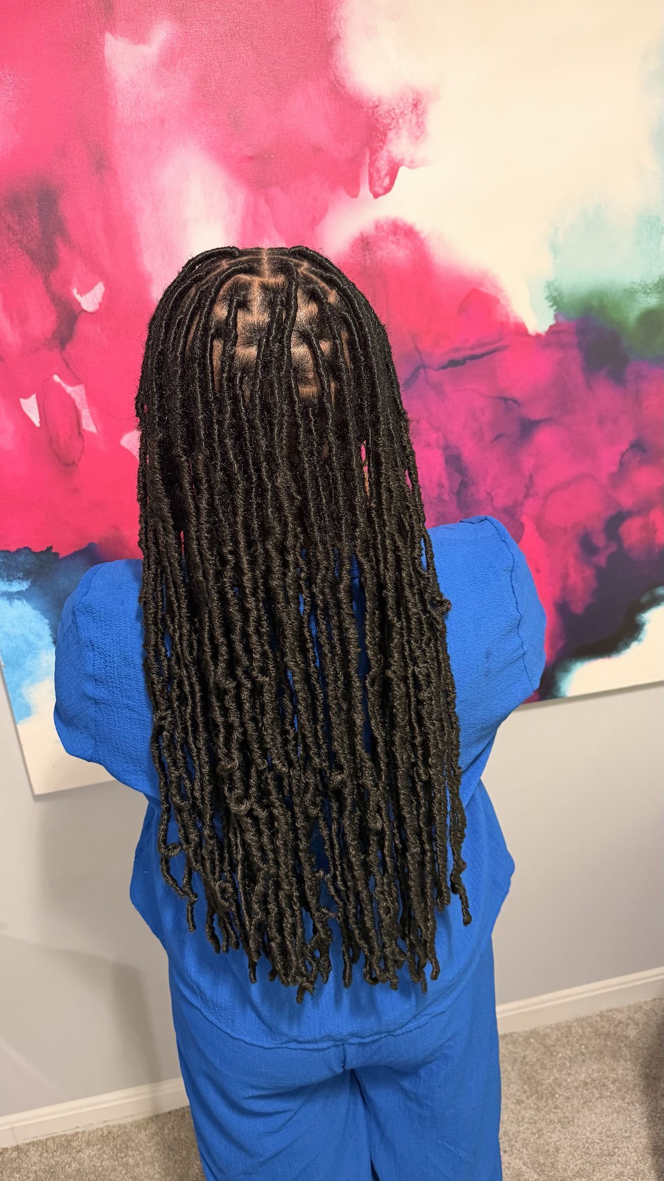 Person with long braided hair in blue clothing facing a colorful abstract painting.