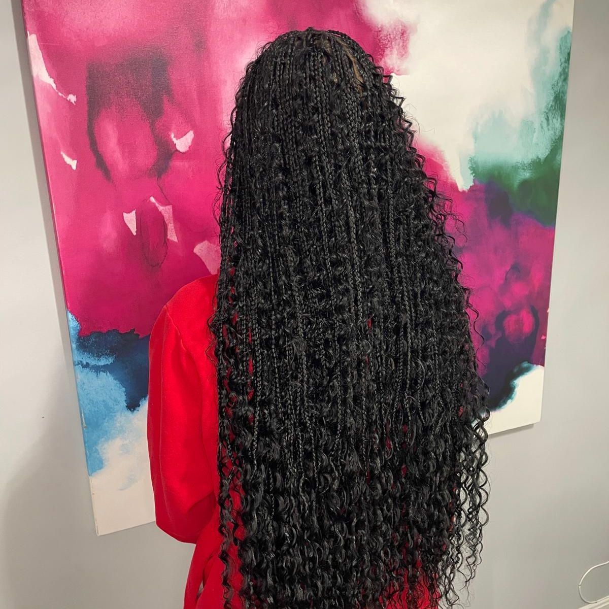 Person with long black braids in a red top standing before a colorful abstract painting