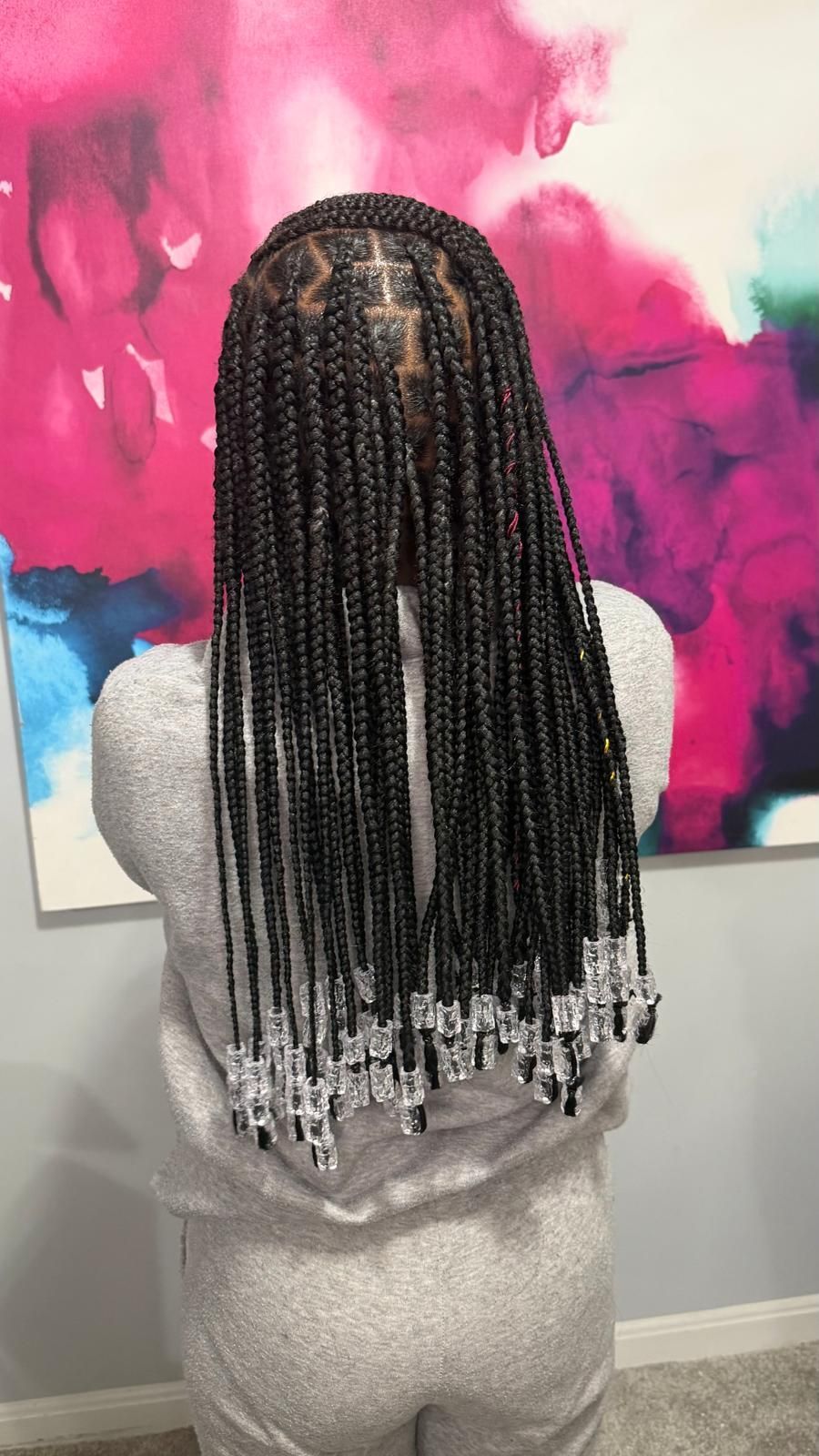 Person with long braided hair facing a pink and green floral wall, wearing a neon yellow top.