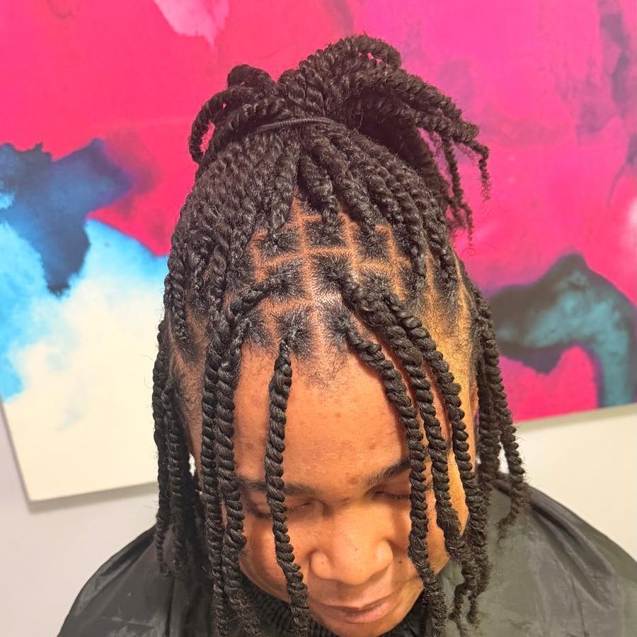 Close-up of braided hair styled in a top bun against a pink and blue abstract wall.