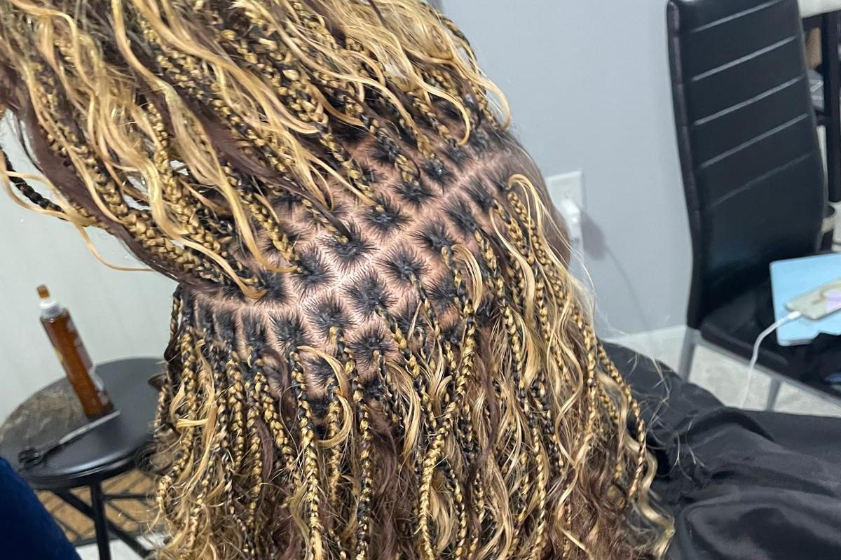 Close-up of braided blonde hair with a visible scalp pattern against a black chair in a salon setting