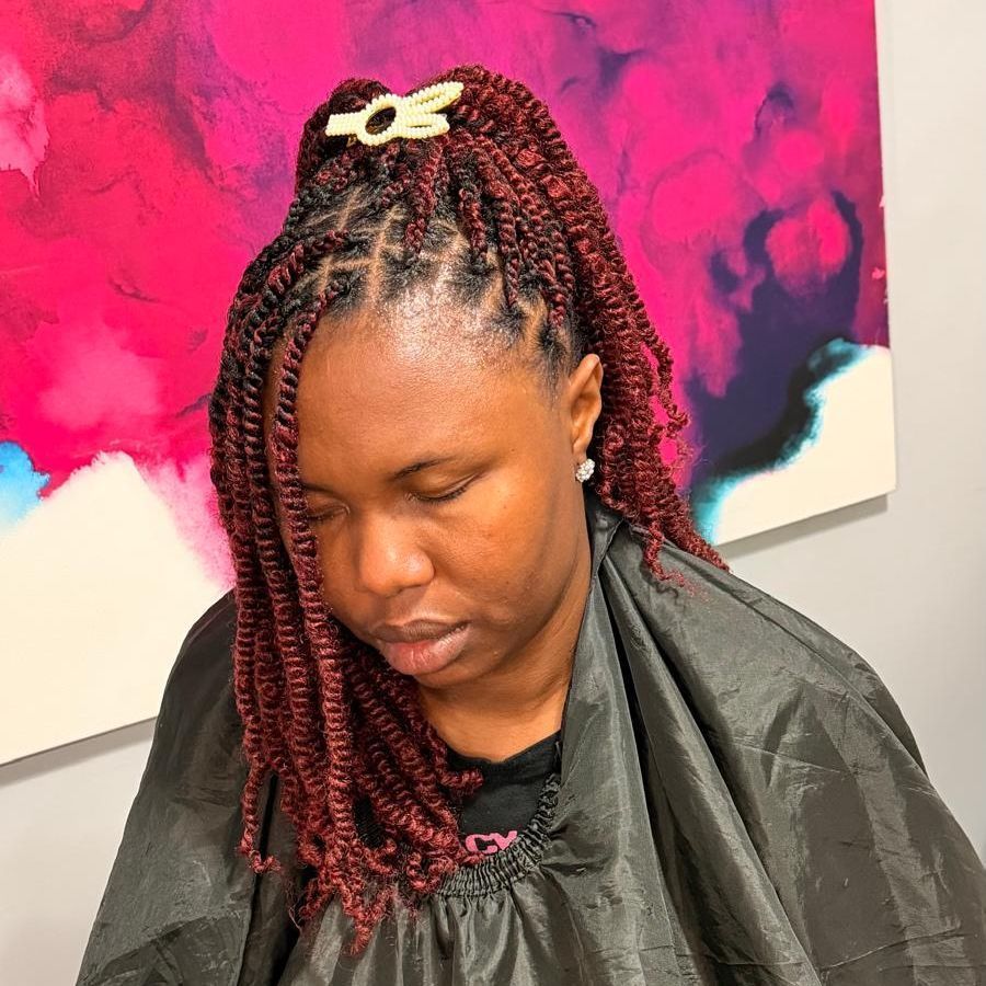 Person with braided hair looking down, wearing a dark jacket against a bright pink abstract background
