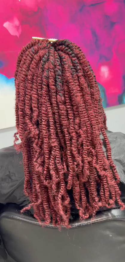 Long maroon braided hairstyle cascading over the back of a black chair against a pink background