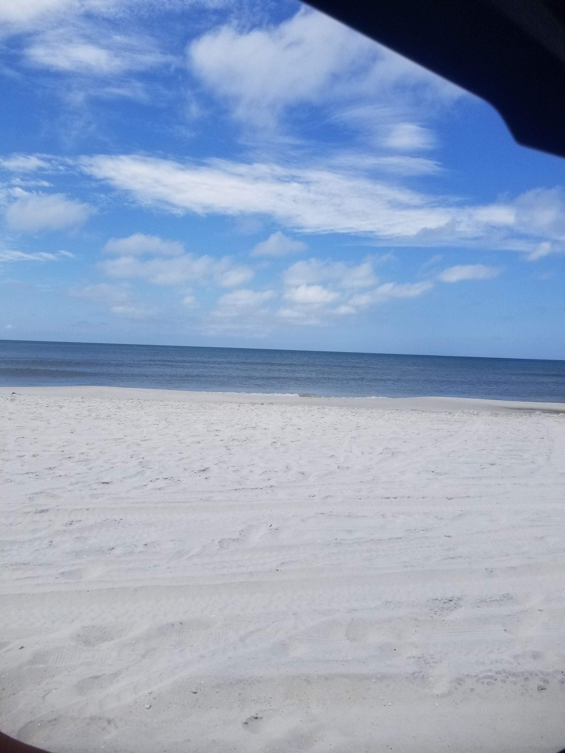 Sandy beach meets blue ocean under a partly cloudy sky.