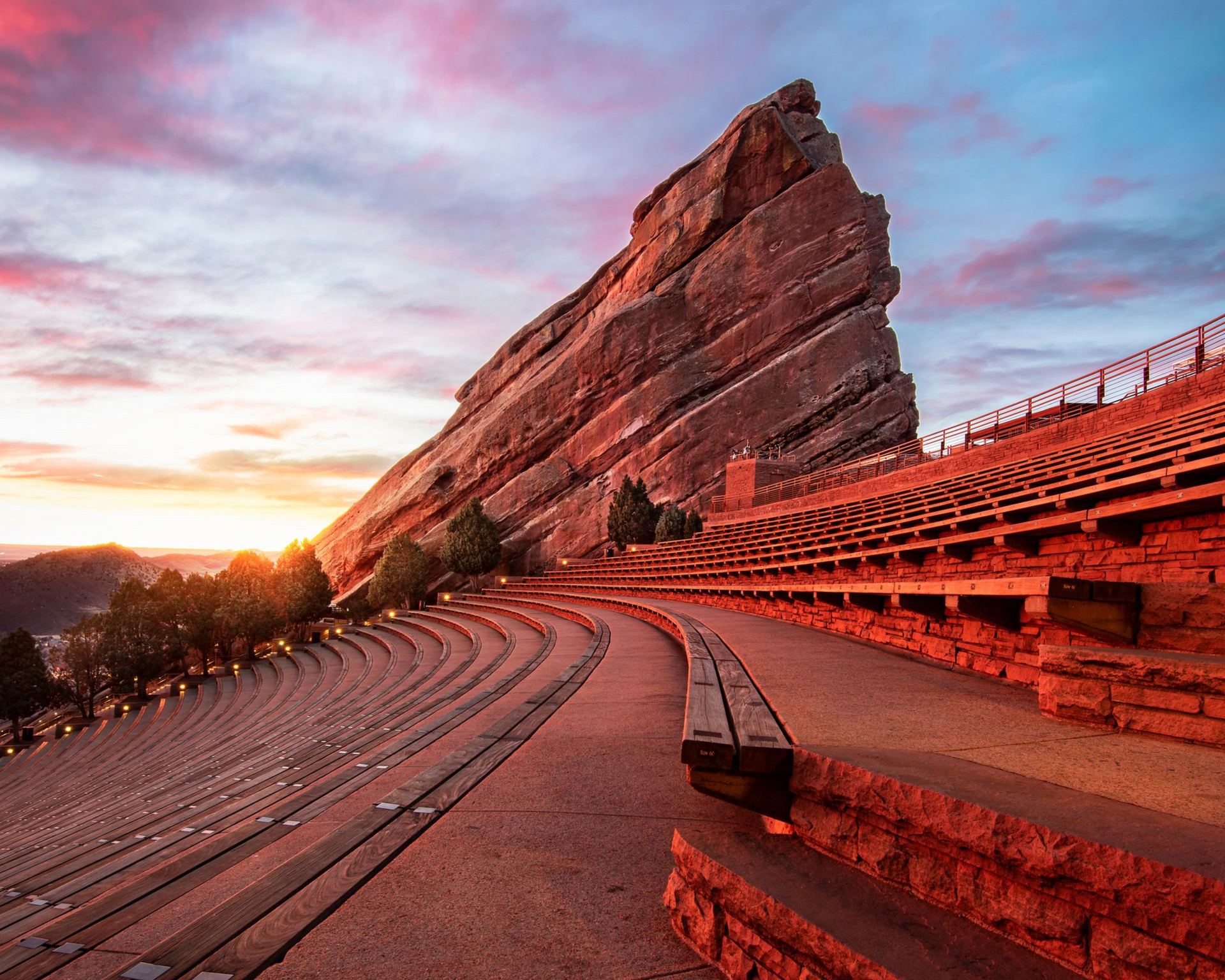 Red sandstone amphitheater at sunset with rows of curved seating and a dramatic rocky backdrop
