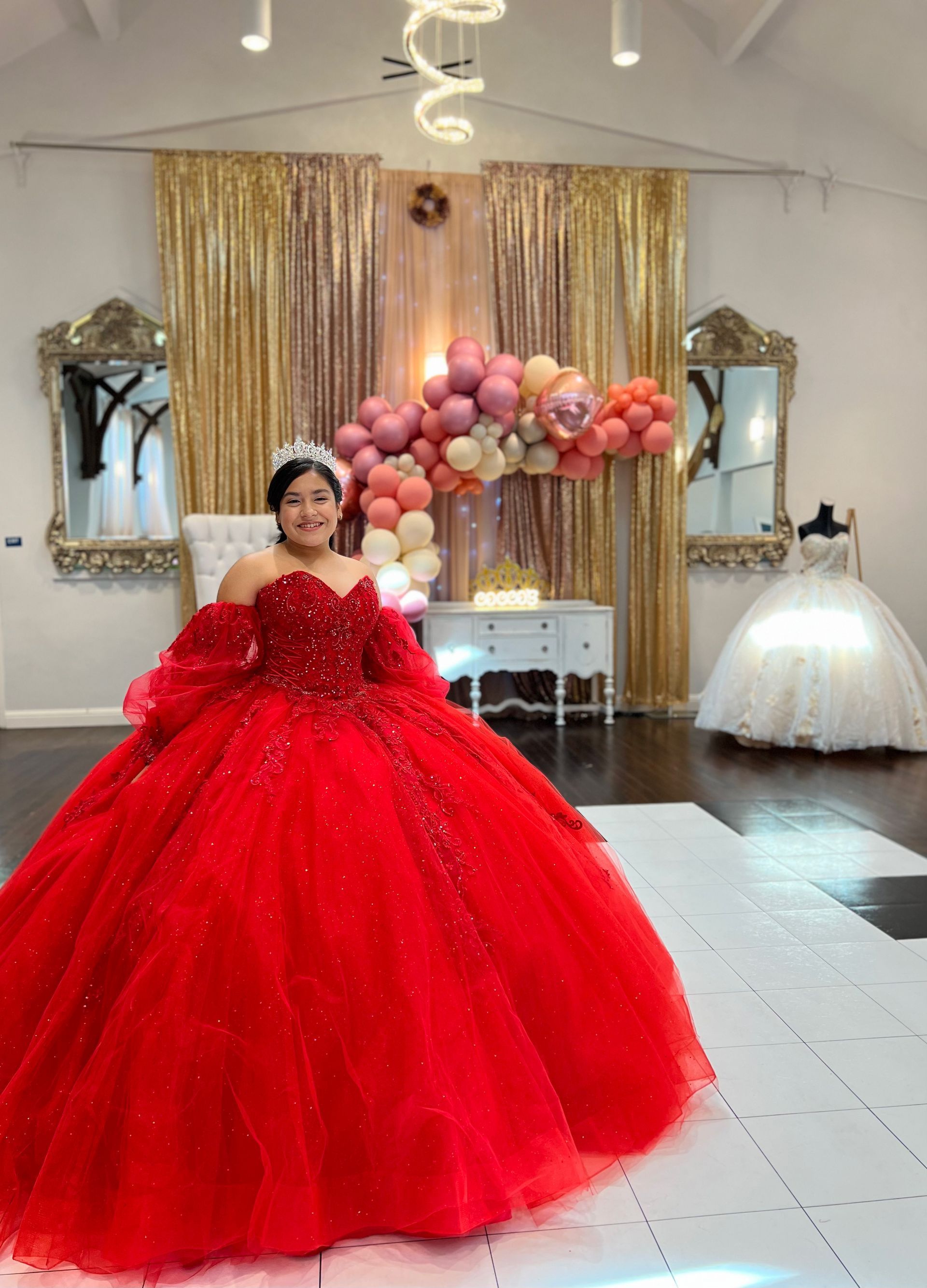 a woman in a red ball gown is standing in a room with balloons .