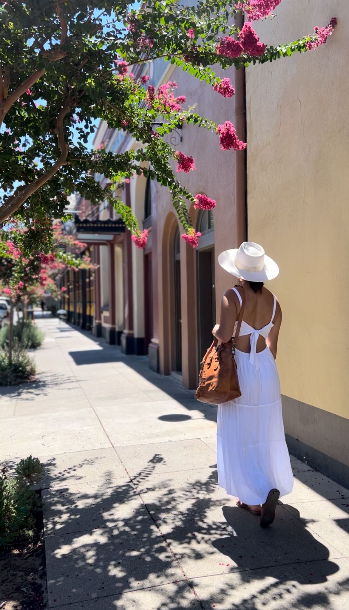 a woman in a white dress and hat is walking down a sidewalk .