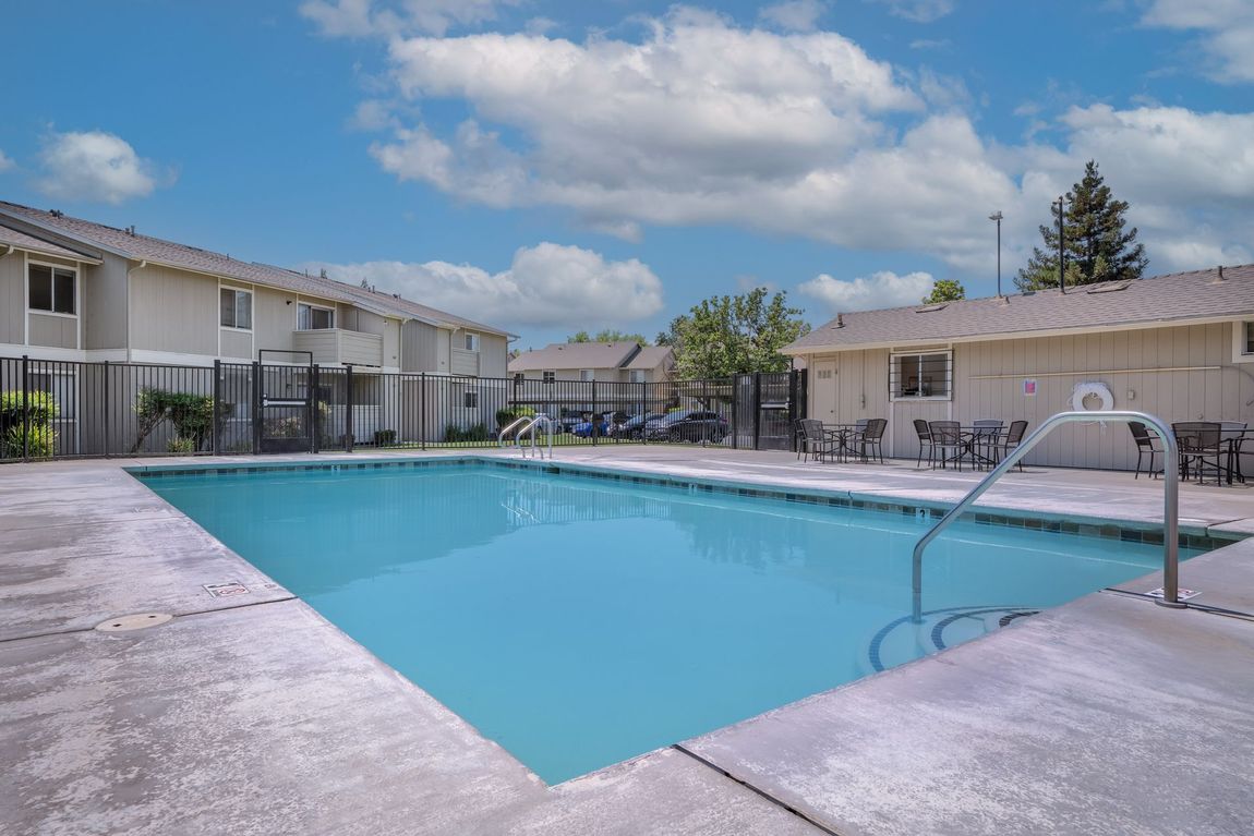 Swimming pool in courtyard of apartment complex under a partly cloudy blue sky.
