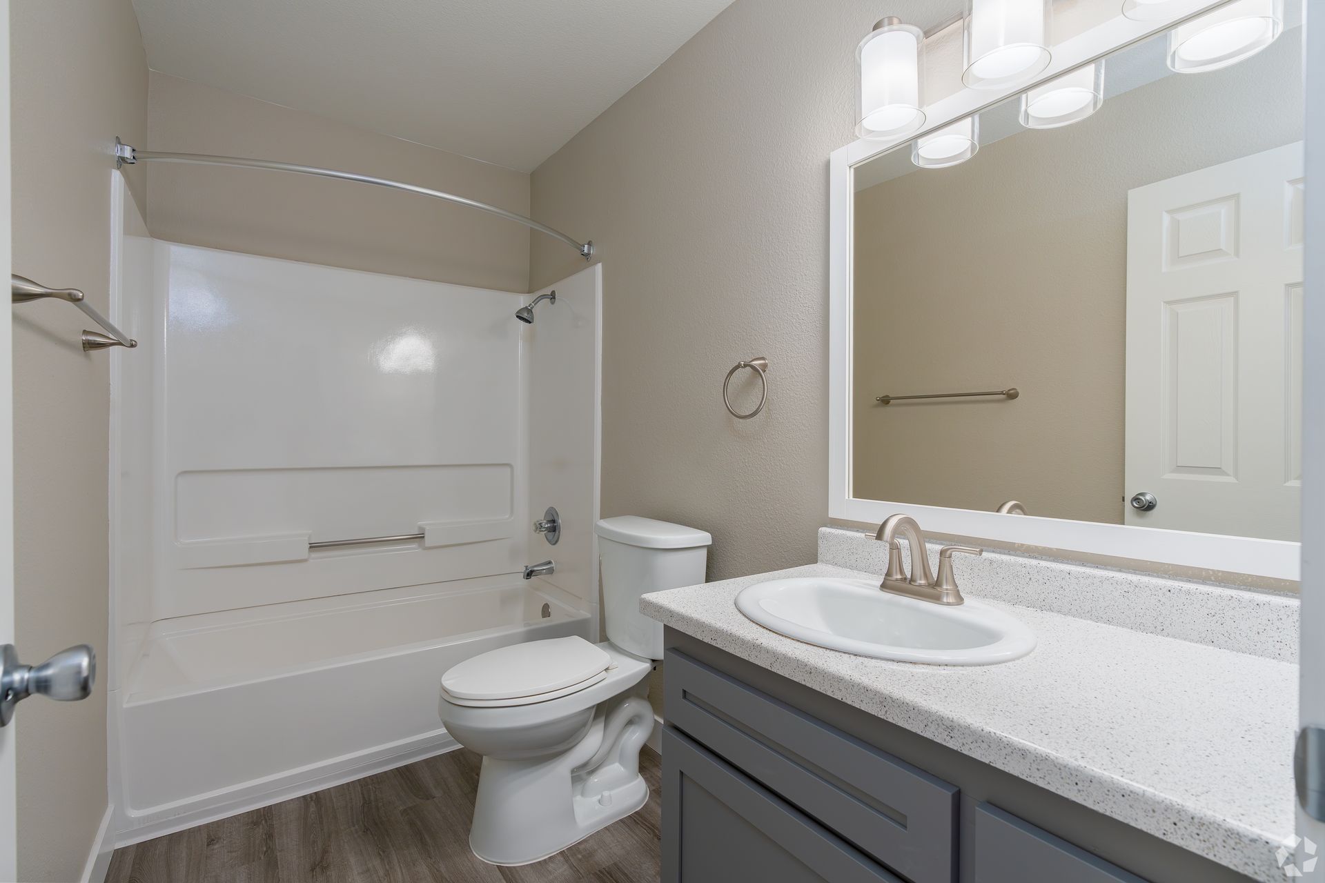 Bathroom with white bathtub, toilet, gray vanity, and large mirror.