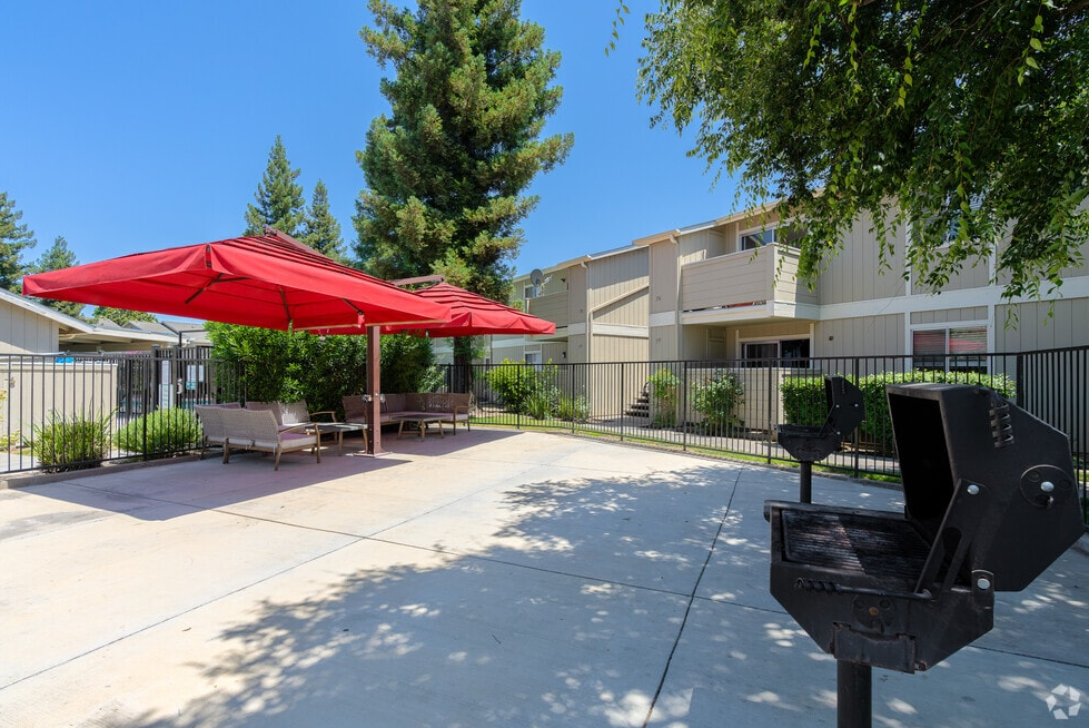 Outdoor apartment patio with red umbrellas, seating, and a grill.