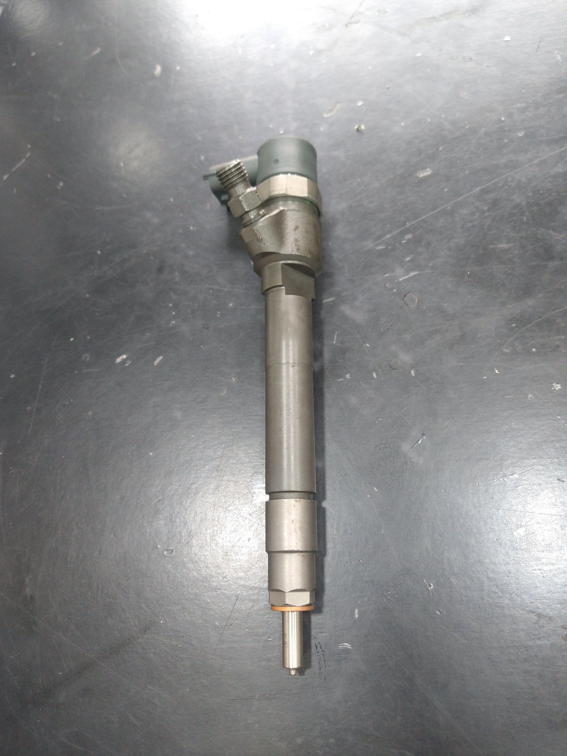 Inyector de combustible, cilindro metálico con boquilla y conector eléctrico, sobre superficie oscura.