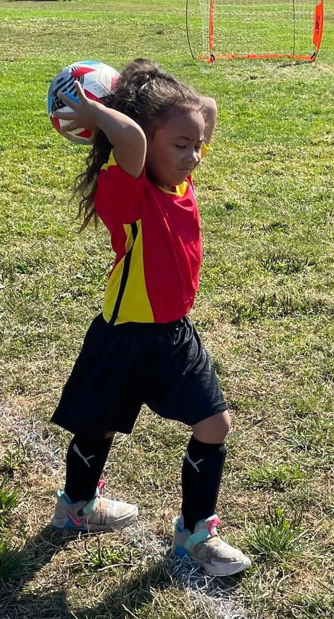 A little girl is holding a soccer ball on a field.