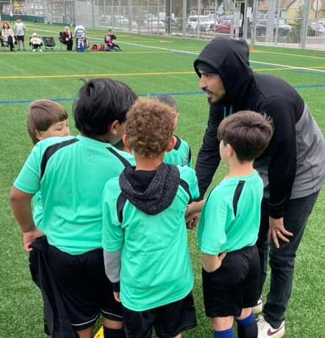 Coachis talking to a group of young boys on a soccer field.