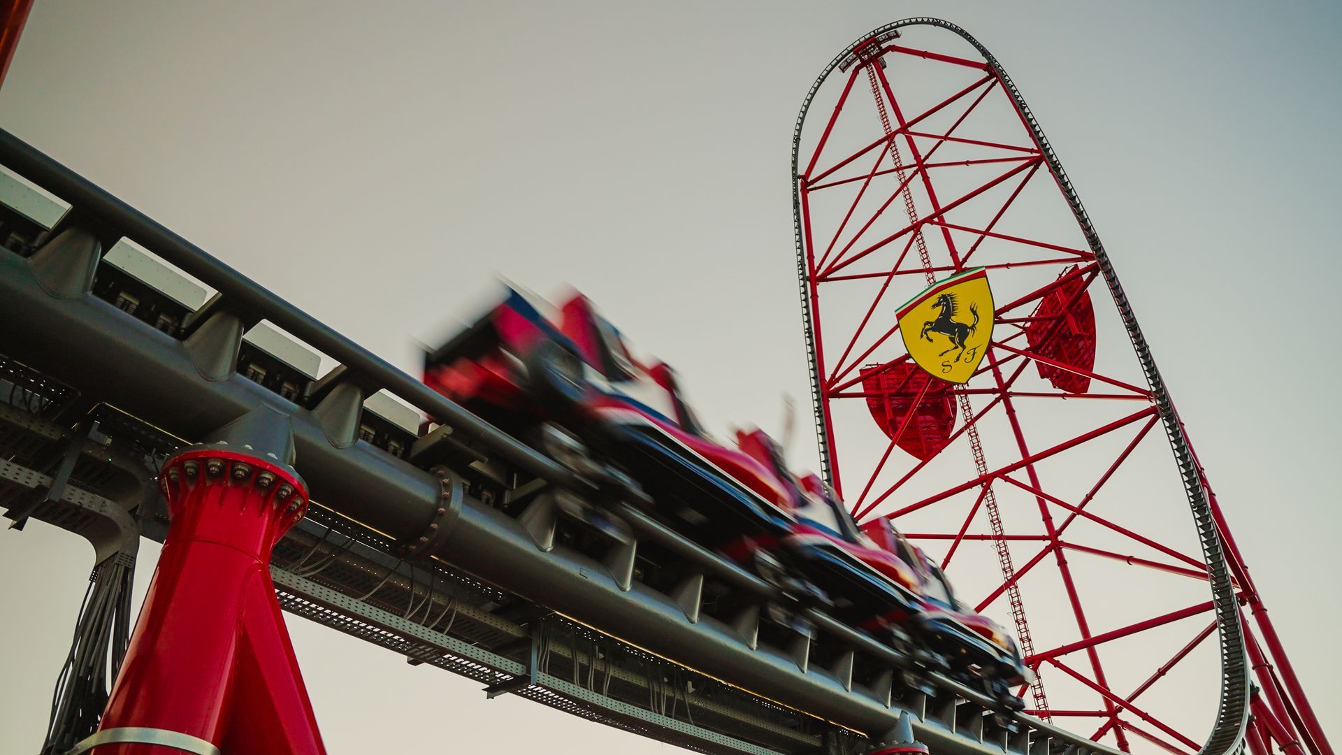 Red Ferrari roller coaster car speeding uphill toward a tall red support structure with the Ferrari logo.