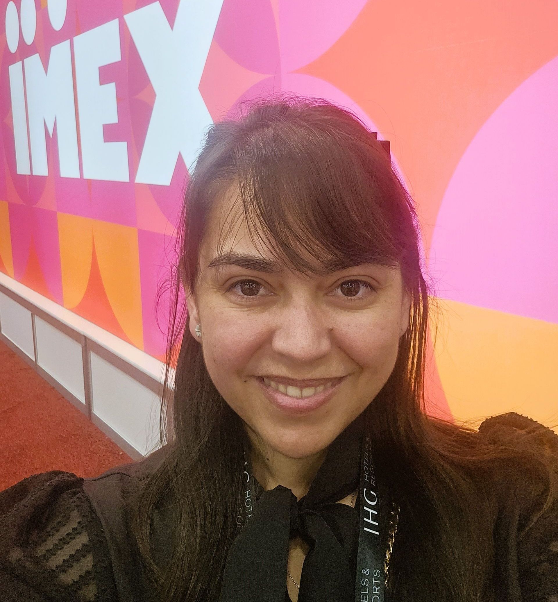 Woman with dark hair and bangs smiles in front of a colorful IMEX backdrop.