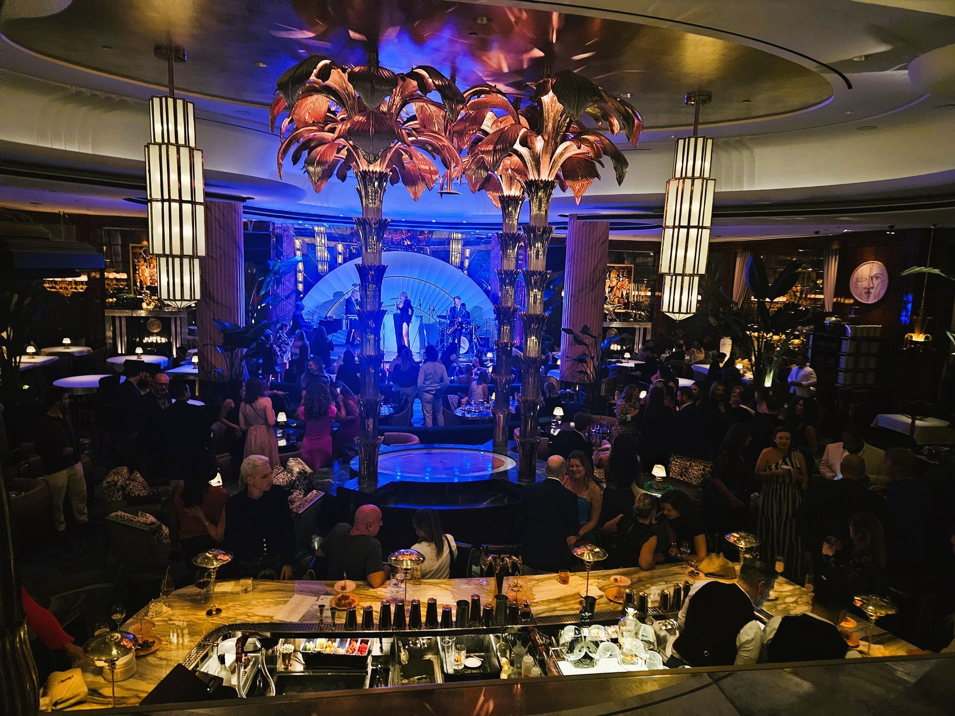 People at a dimly lit bar, with a band performing on stage and decorative lights.