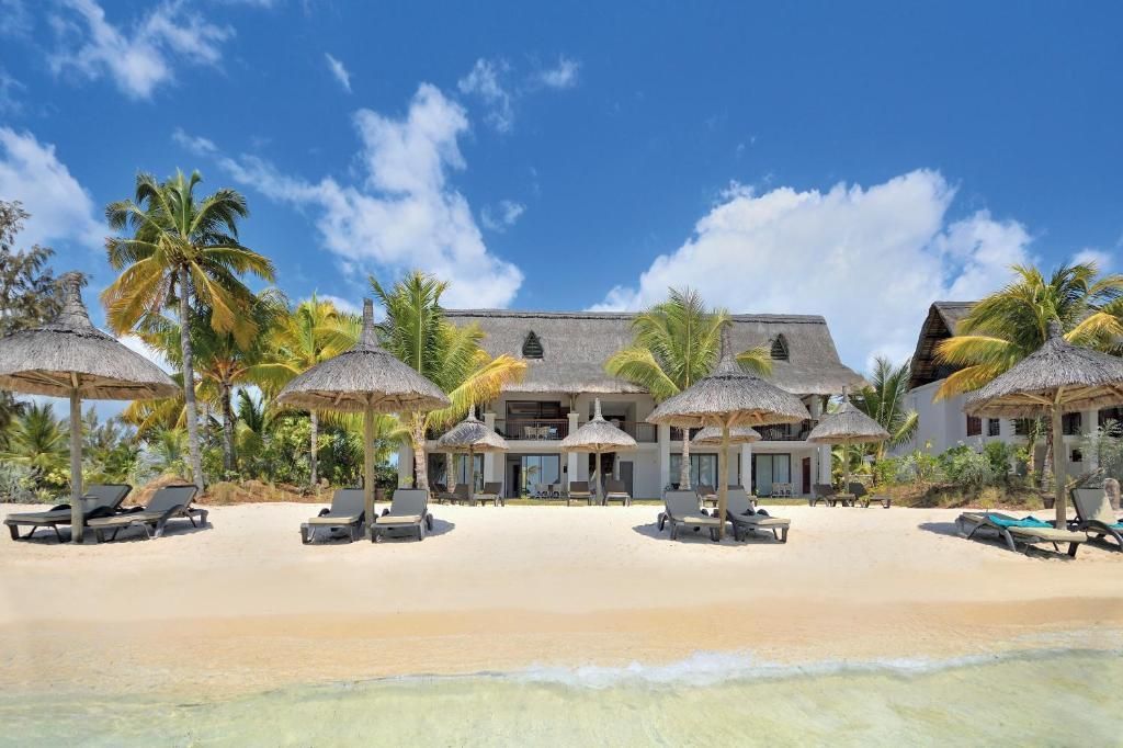 Beachfront resort with thatched umbrellas, lounge chairs, and a blue sky.