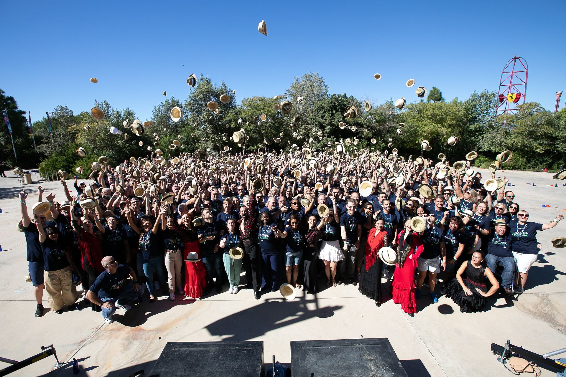 Large group of people outdoors throwing hats in the air on a sunny day.