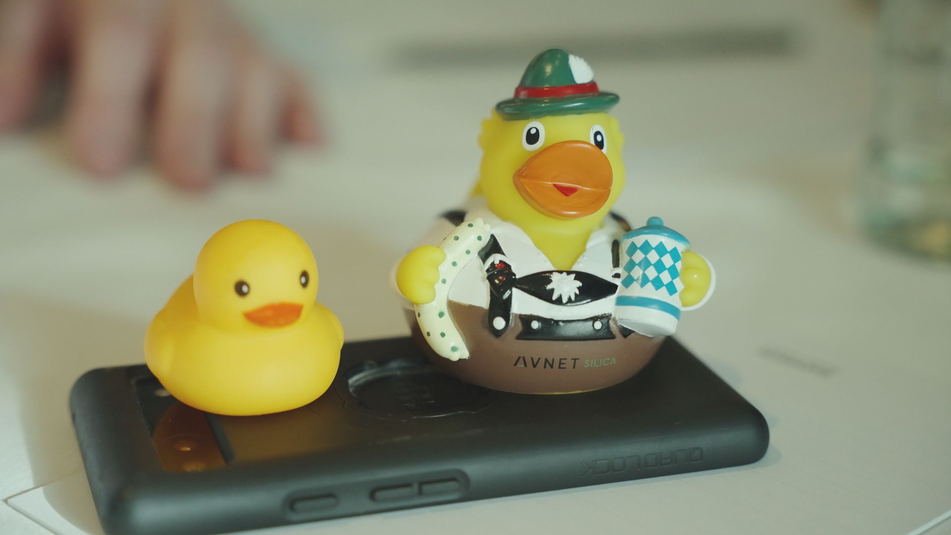 Two rubber ducks, one plain yellow, the other in Bavarian attire, on a phone case.