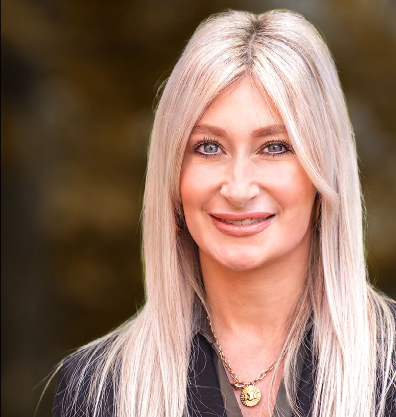 Blonde woman wearing a leopard print jacket smiling outside.
