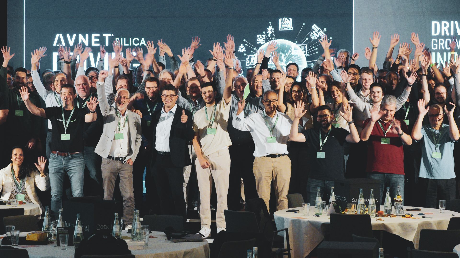 Group of people at a conference raising arms in celebration, the banner says
