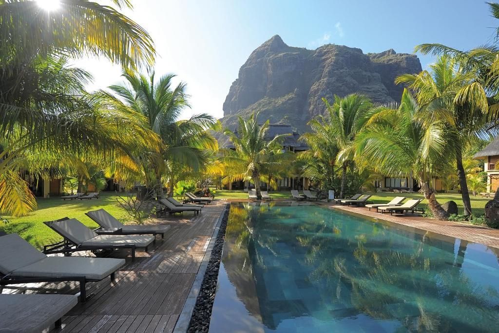 Pool with lounge chairs, palm trees, and mountain backdrop. Sunny, tropical setting.