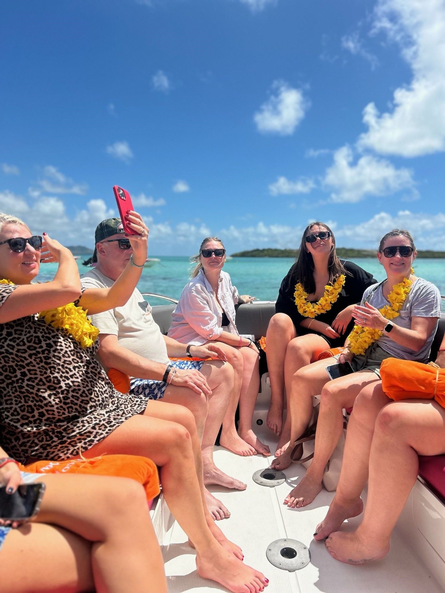 Group of people on a boat, taking selfies under a blue sky. Ocean and islands are in the background.