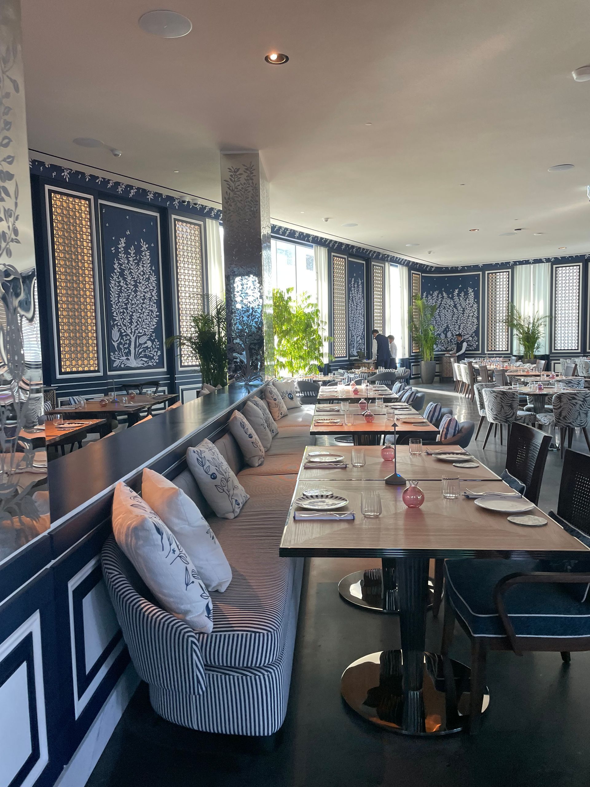 Restaurant interior with blue and white decor, tables set, and natural light streaming in.