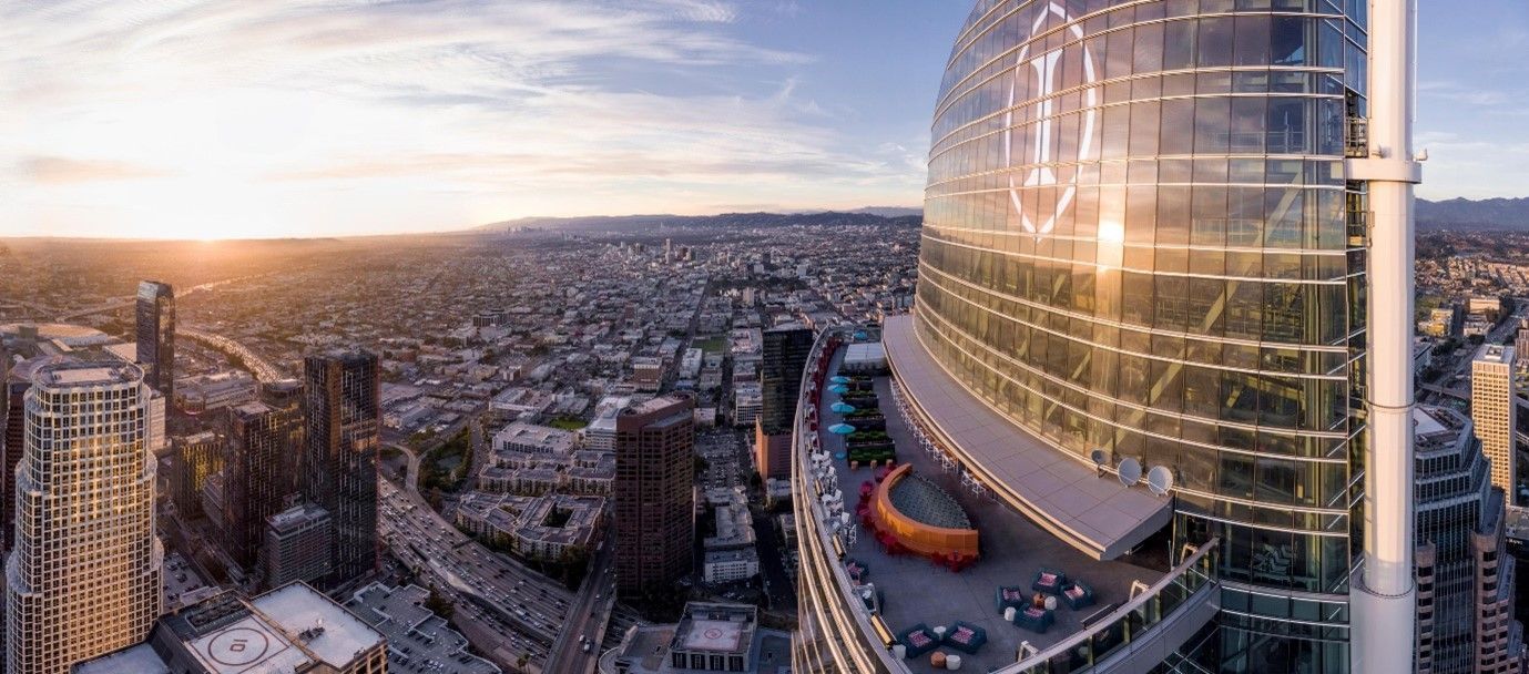 Panoramic view of a city skyline with skyscrapers and a rooftop patio at sunset.