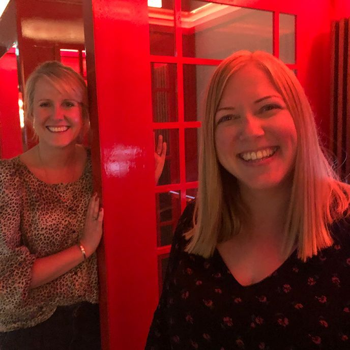 Two smiling women pose in front of a red booth with the woman on the right in a navy shirt.