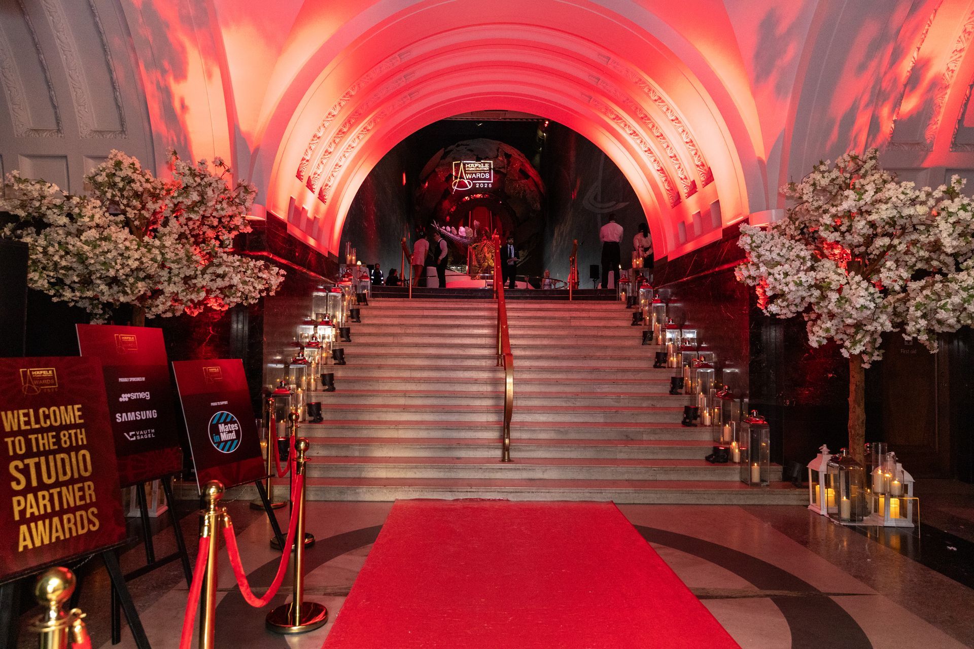 Red carpet leading up grand staircase to awards event entrance. Red and white flowers flank sides.