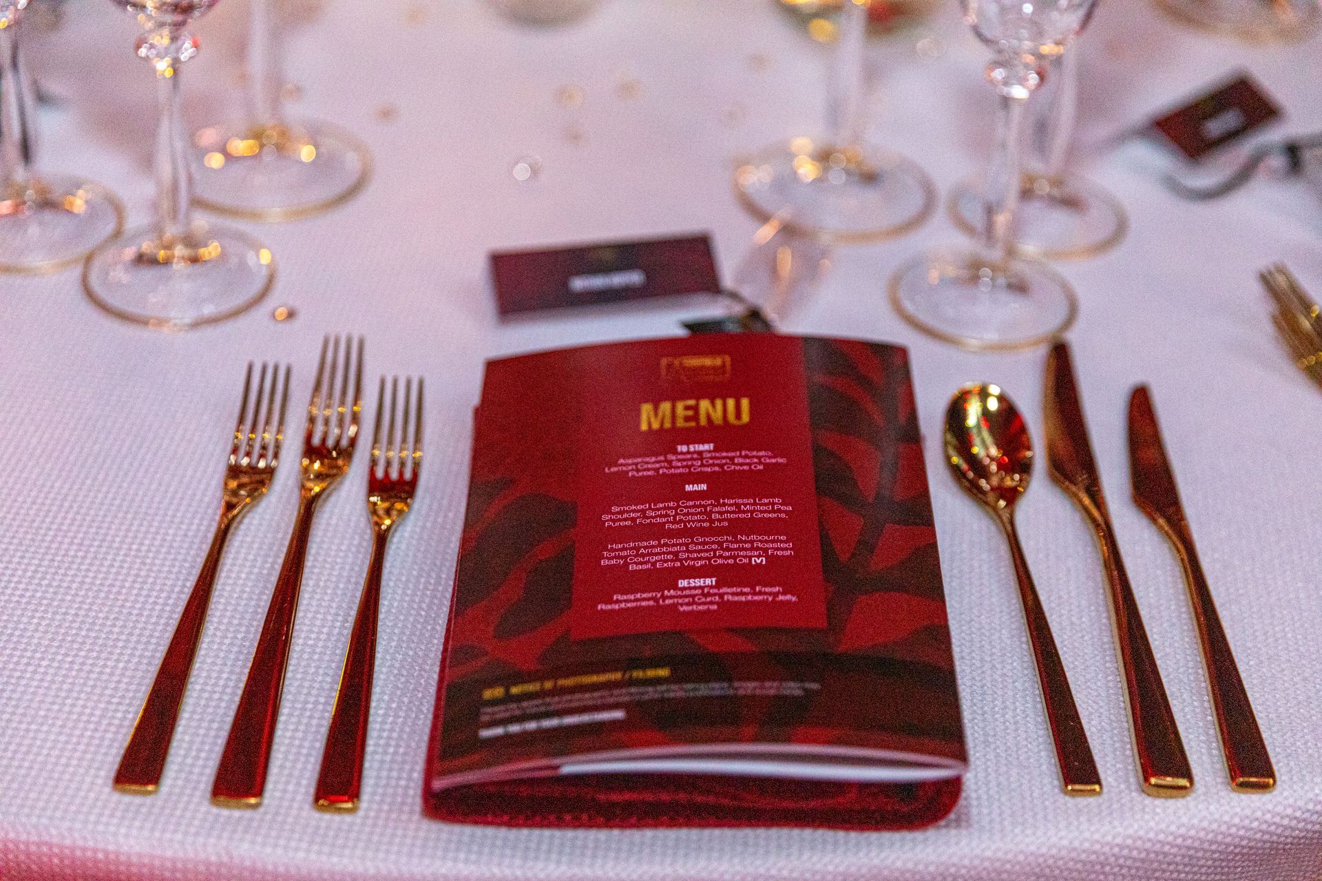 Formal table setting with gold flatware, wine glasses, and a red menu.