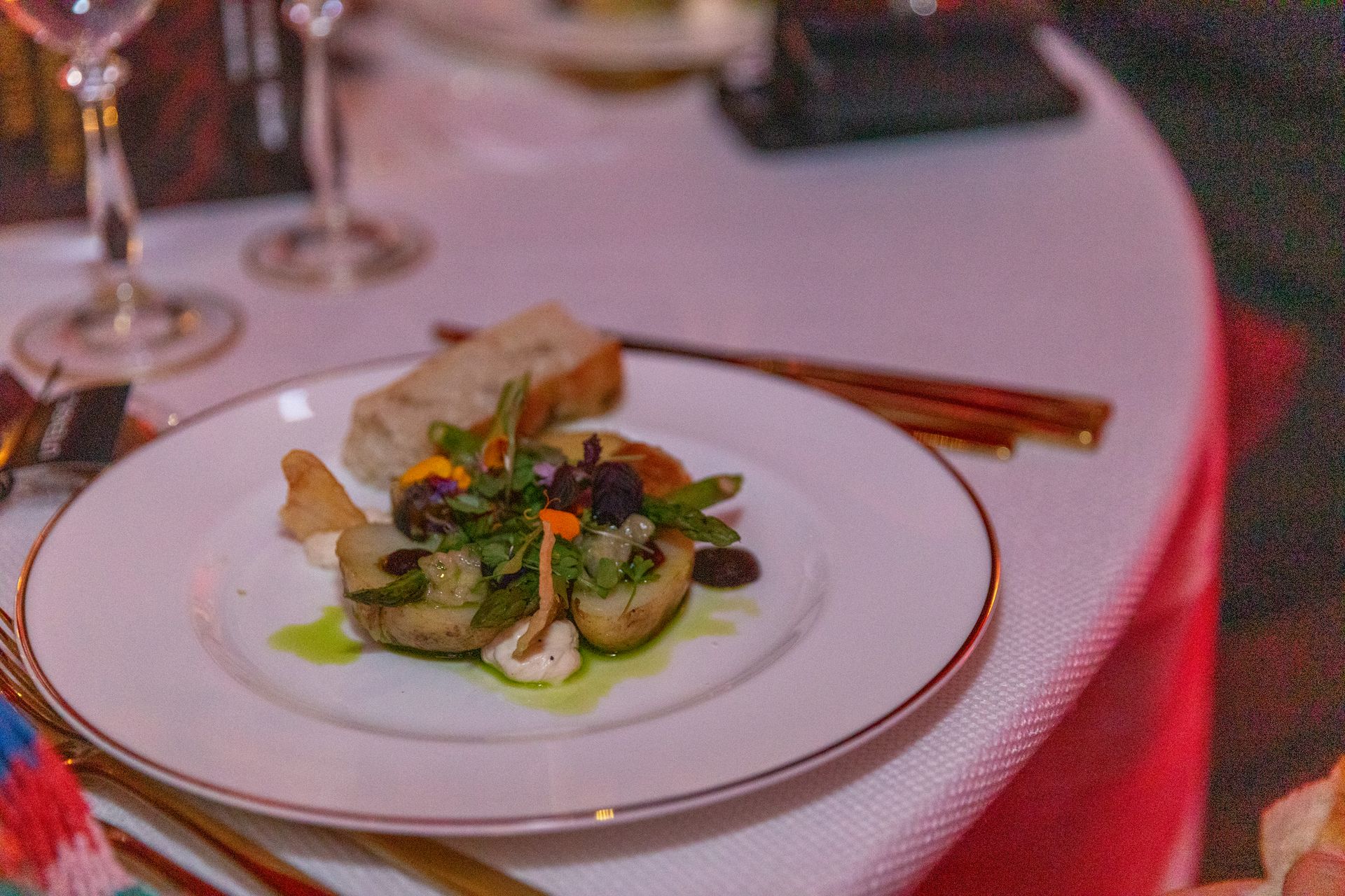 Plate of food on white tablecloth, with bread, vegetables, and garnishes.