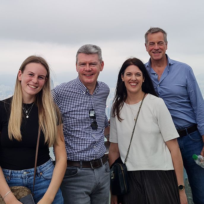 Four people smiling on a cloudy day, overlooking a city.