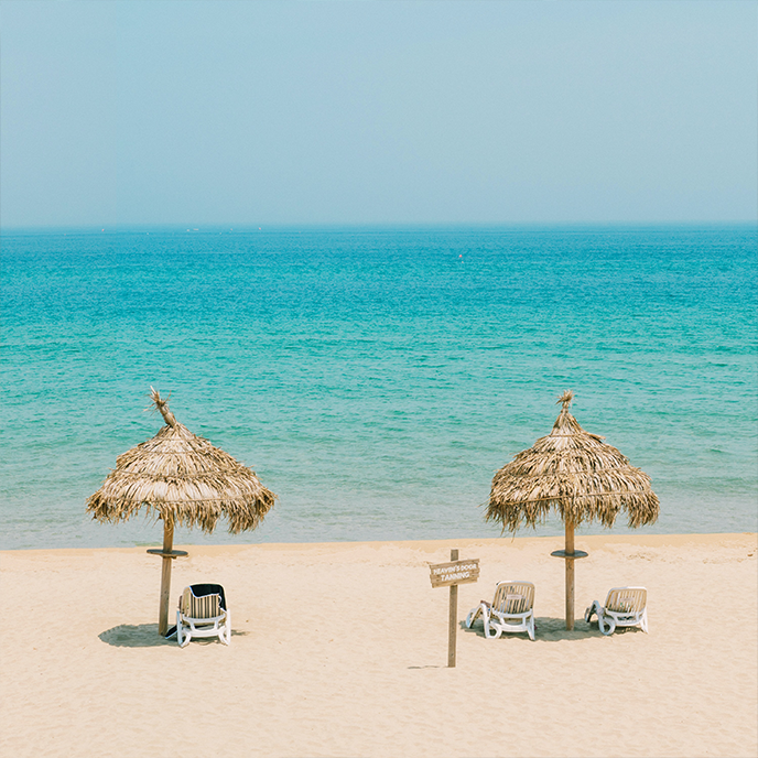 Beach scene with two straw umbrellas, lounge chairs, and turquoise water.