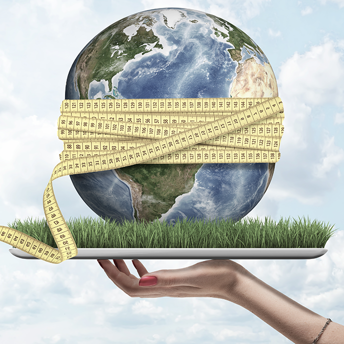 Earth wrapped in a measuring tape, held on a tray of grass by a hand. Sky background.