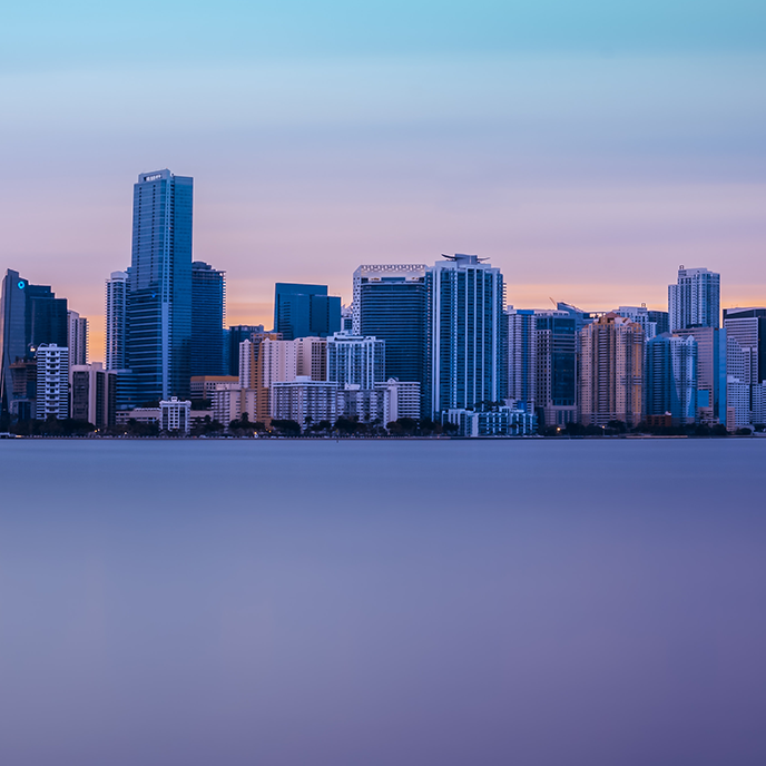 Miami skyline at dusk, with colorful sky and still water.