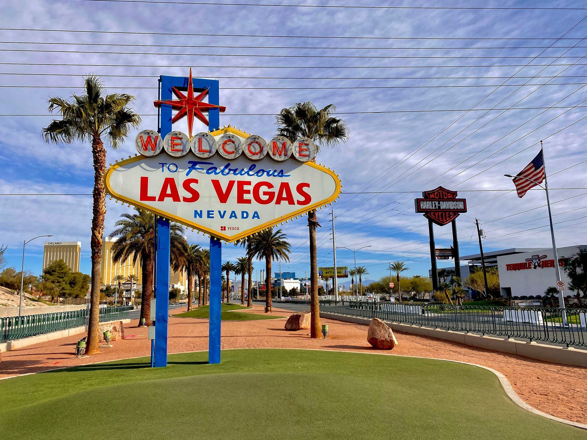 Las Vegas welcome sign with blue sky, palm trees, and the American flag in the background.