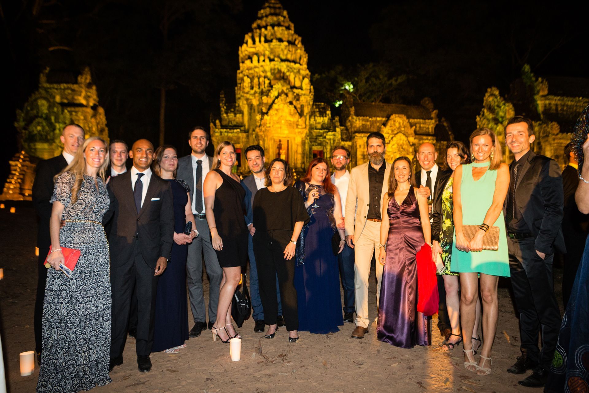 Group of people in formal attire pose in front of illuminated temple at night.
