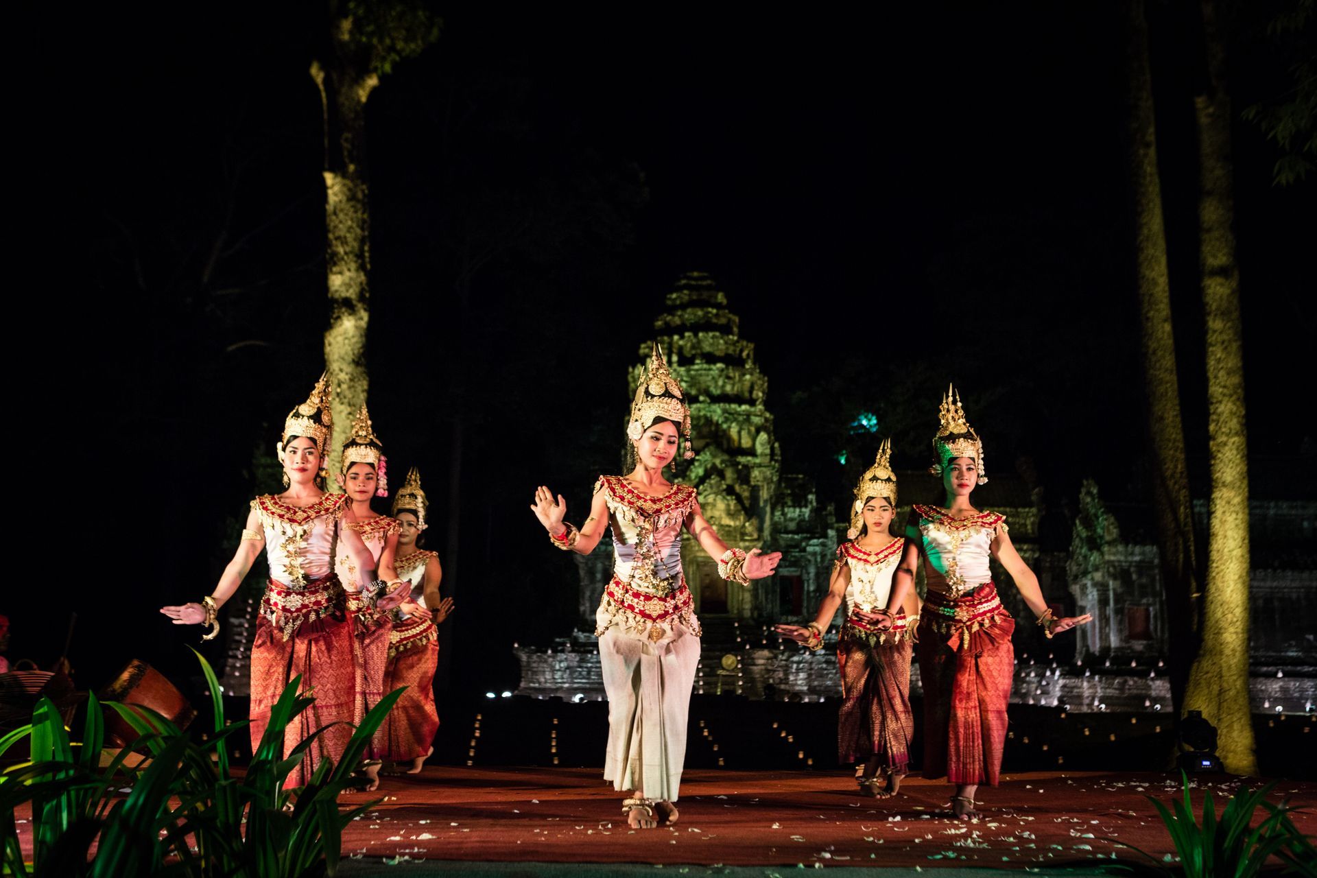 Dancers in traditional Cambodian costumes perform in front of Angkor Wat at night.