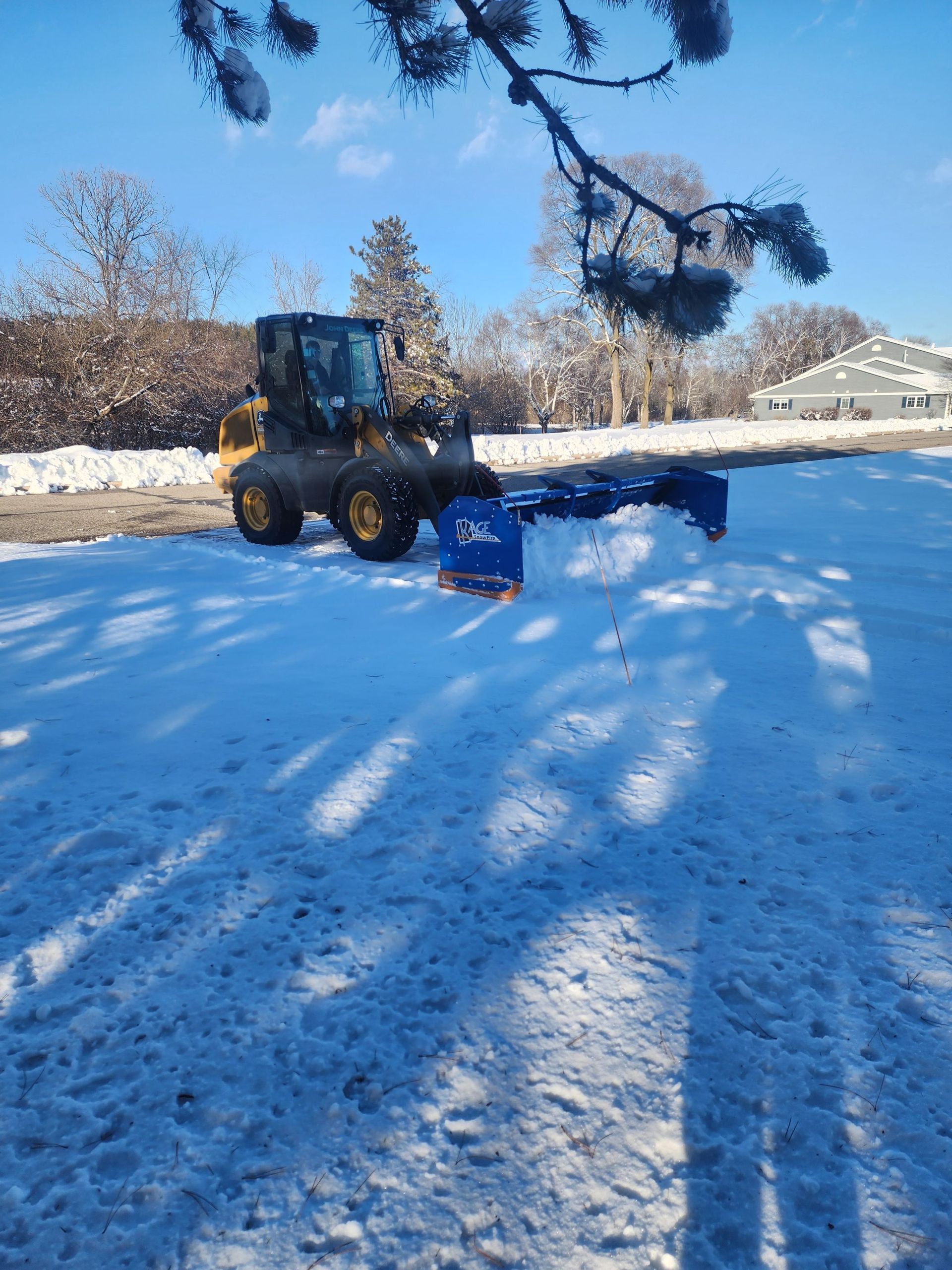 Two workers in bright safety gear clearing snow on a path in a snowy wooded area
